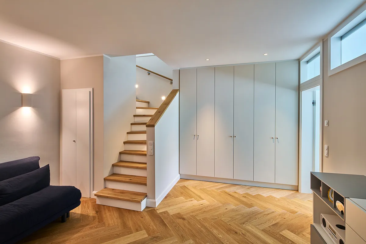 Untergeschoss einer Maisonettewohnung mit integrierten Einbauten, Eichenparkett im Fischgrätmuster und Treppe mit Holzstufen und Lichtleiste.